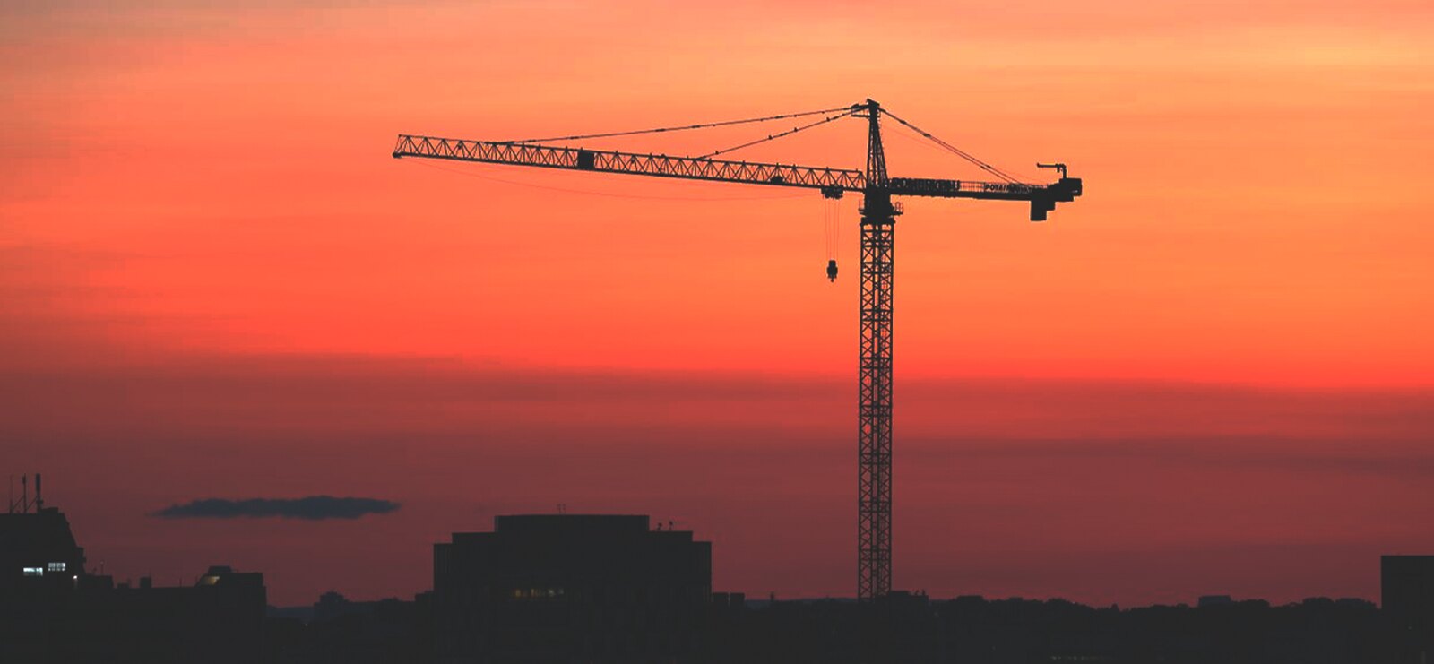 Grúa torre al atardecer sobre la silueta de una ciudad
